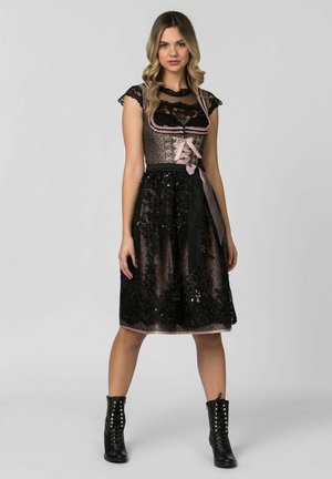 Spitzen- und Satinkleid mit tailliertem Oberteil, in Rosa- und Schwarzfarben gehalten, mit Paillettenrock und einem schwarzen Taillengürtel. Knöchelhohe Stiefel runden den Look ab.
