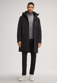 Czarna ocieplana parka z odpinanym kapturem, zapinana na zamek i zatrzask, zestawiona z szarym golfem i czarnymi spodniami, noszona z białymi sneakersami.