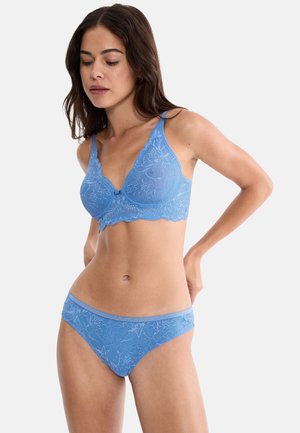 Frau trägt hellblauen Spitzen-BH und passende Pantys, steht mit einer Hand am Rücken und blickt nach unten.