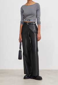 Grå ribbad kort topp med båtformad halsringning, kombinerad med höga svarta läderbyxor med vida ben. Inkluderar ett svart bälte och en handväska.