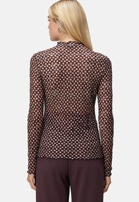 Haut à manches longues en tissu en maille noir et cuivre avec un motif géométrique texturé et un ourlet festonné, associé à un pantalon sombre.