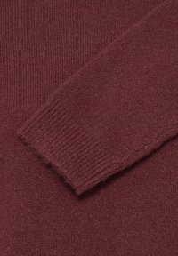 Gros plan sur la manchette côtelée douce d'un pull en tricot grenat montrant la texture du tissu et le détail des points.