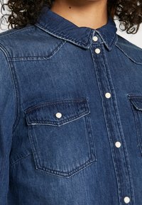Denim overhemd met een gekleed hals, blauwe kleur, twee borstzakken met knoopaccenten en contrasterende stikdetails.
