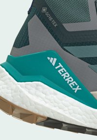 Grau und türkisfarbene Wanderschuhe mit Gore-Tex-Obermaterial, strukturiertem Mesh und einer dicken weißen Zwischensohle. Merkmale sind das "TERREX"-Logo und eine robuste Gummisohle.