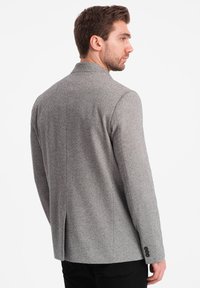 Grå hundtand mönstrad kavaj med slagkrage, en slits bak och knäppta manschetter. Tillverkad av textil, skräddarsydd passform.