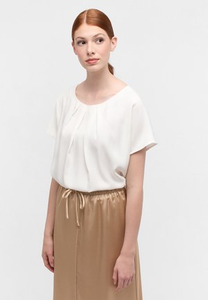 Weiße Bluse mit kurzen Ärmeln, runder Ausschnitt und Falten. Kombiniert mit einem beigen Satinrock mit elastischem Bund und Kordelzug.