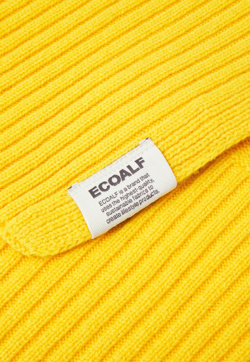 Jasnożółta prążkowana tkanina z białą metką marki ECOALF, informującą o jej zastosowaniu wysokiej jakości tkanin zrównoważonych.