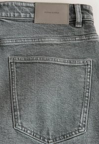 Grå denimjeans med en texturerad yta, med en bakficka och en rektangulär tygskylt präglad med "DENIM SUPPLY."