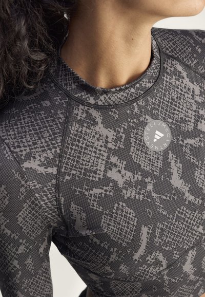 Zbliżenie na osobę ubraną w czarną i szarą sportową bluzkę z okrągłym logo na piersi z napisem Stella McCartney.