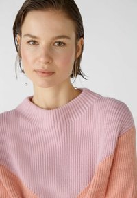 Geribbelde gebreide trui in roze en perzik, met een hoge hals en een kleurblok ontwerp. Gladde textuur met contrasterende mouwen.