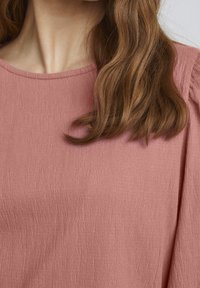Top texturizado rosa con tejido acanalado, escote redondeado y mangas suavemente abullonadas, que muestra un diseño sutil y un acabado suave.