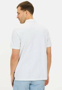 Hvid polo-shirt med korte ærmer og klassisk krave, uden detaljer bagpå og med sideslidser i kanten. Fremstillet af glat, letvægtsstof.