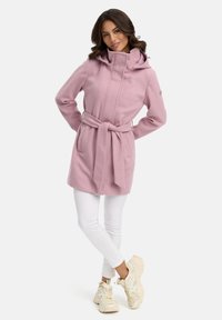 Light pink coat with a high collar, drawstring hood, and tied belt. Long sleeves and side pockets. Worn over white pants and chunky sneakers.