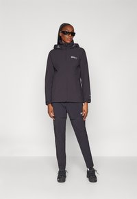 Black waterproof jacket with a hood and zip closure, paired with matching pants. Both feature logo accents and a sleek, fitted design.