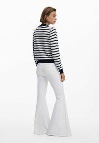 Gestreifter Pullover in Marineblau und Weiß, aus gestricktem Stoff mit gerippten Bündchen, kombiniert mit weißen, ausgestellten Jeans, die eine subtile Nahtdetails an der Seite aufweisen.