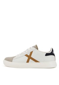 Baskets basses blanches avec bout en daim beige, détail latéral beige formant un X, lacets blancs et languette de talon noire avec logo.