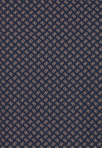 Marineblauer Stoff mit einem sich wiederholenden geometrischen Muster in Creme und Hellbraun. Das Design besteht aus ineinandergreifenden Formen mit kleinen Details.