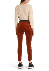 Pantalon en velours côtelé couleur rouille, coupe slim, taille haute avec poches arrière, associé à un haut à manches longues beige clair et des baskets noires.