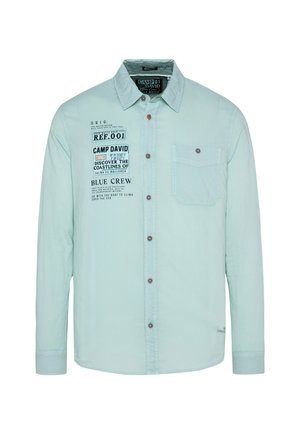 Camisa de manga larga en verde menta claro con cierre de botones y bolsillo en el pecho. Presenta texto impreso y un cuello en contraste. Fabricada con una tela suave.