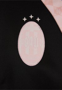 Črn material z ovalnim roza izvezenim logotipom z dvignjenimi črkami, ki ga nadomeščajo tri majhne bele zvezde.