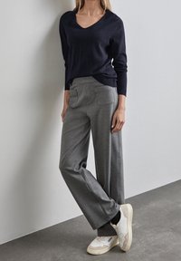 Marinvänlig v-ringad tröja i mjukt stickat material, matchad med gråvida byxor med bred benlängd och sydda fickor. Skor: vita och beige sneakers.