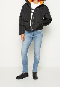 Doudoune noire avec doublure orange, poignets côtelés et fermeture éclair, associée à un jean skinny bleu clair et des bottines noires.