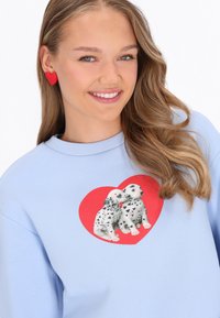 Sudadera azul claro con un gráfico de un corazón rojo y dos cachorros dálmatas. La tela es suave, con cuello redondo y puños acanalados.