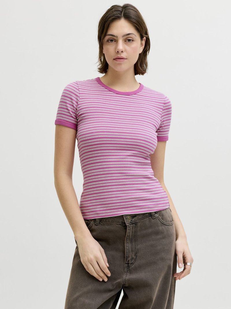 Young woman wearing a pink and white striped short-sleeve shirt and dark gray pants, standing against a plain light background.