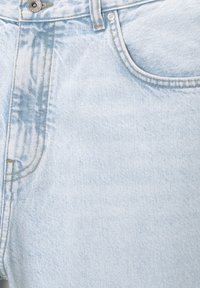 Vaaleansininen farkkukangas, jossa on hieman haalistunut tekstuuri. Siinä on näkyvä nappi ja ompeluyksityiskohdat taskuissa ja saumoissa.