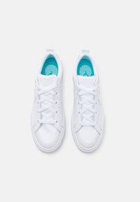 Zapatillas blancas con parte superior sintética y suave, puntera redonda y plantilla azul texturizada. Incluyen cordones tradicionales y un tirador de talón reforzado.
