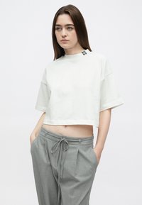 Krátke biele tričko z jemnej bavlny s krátkymi rukávmi a čiernym logom "HUGO" na výstrihu. Kombinované so svetlosivými nohavicami.