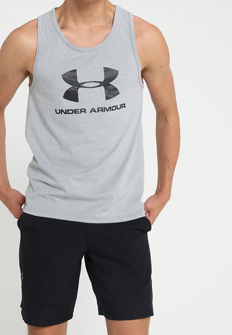 Camiseta atlética sin mangas gris con el logo negro de "Under Armour", combinada con pantalones cortos negros de material texturizado y con bolsillos.