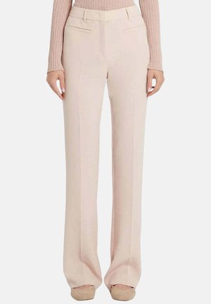 Vrouw draagt lichtbeige, wijd uitlopende broek met hoge taille, gecombineerd met beige platte schoenen en een geribde roze top met lange mouwen.