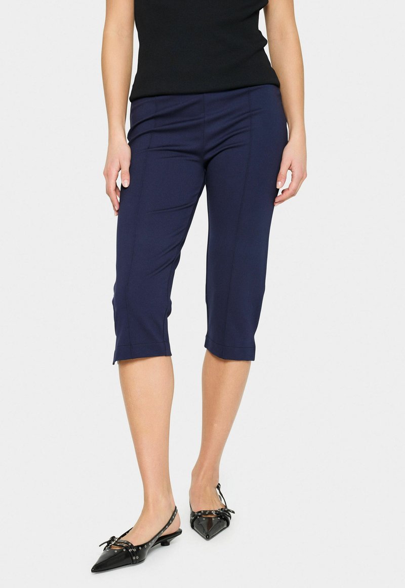 Navy stretch capri pants with a fitted design, cropped length, and a smooth texture, paired with black patent slingback shoes.