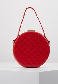 Červená kulatá kabelka vyrobená z prošívané umělé kůže, s vrchním uchem a zlatými detaily. Hladký povrch s diamantovými vzory.