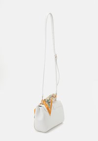 Biała torebka z eko skóry o wyraźnej strukturze, z regulowanym paskiem oraz dekoracyjnym pomarańczowym szalikiem z motywem kwiatowym, zawiązanym na górze.