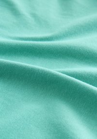 Měkká tkanina v tyrkysové barvě se hladkým povrchem a mírným leskem, s jemně tkaným vzorem a jemným padáním.