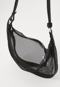 Černá síťovaná kabelka s měkkým, zakřiveným tvarem. Obsahuje zipové zapínání a nastavitelné popruhy, vyrobená z lehkých materiálů.