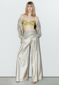 Metallic sølv brede bukser parret med en grøn satin bralette, suppleret af en matchende sølv oversized blazer med tekstureret stof.