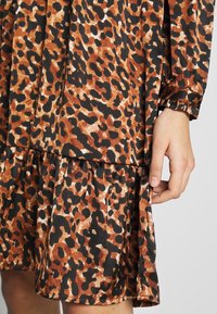 Klänning med leopardmönster i nyanser av brunt, svart och kräm. Tyget har en mjuk textur, med en volang nertill och utsvängda ärmar.