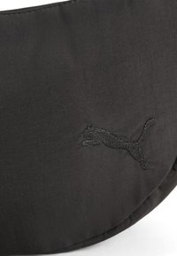Czarna czapka z tkaniny o teksturowej powierzchni, z haftowanym logo Puma w czerni. Zakrzywiony kształt; minimalistyczny design.