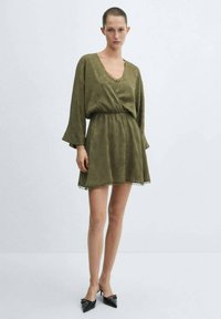 Robe mini vert olive avec un décolleté en V, de longues manches évasées et une taille élastique. Présente des bordures en dentelle à l'ourlet et un tissu doux et texturé.