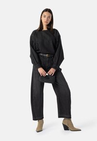 Svart denimtopp med løse ermer, kombinert med høytlivs svarte jeans. Beige ankelstøvletter i semsket skinn med spiss tupp og svart flettet clutch.