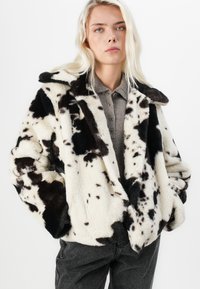 Faux-Fur-Mantel in Creme mit schwarzen und braunen Flecken, mit einem breiten Kragen und lockerer Passform. Strukturiertes, weiches Material mit einem gemütlichen Aussehen.