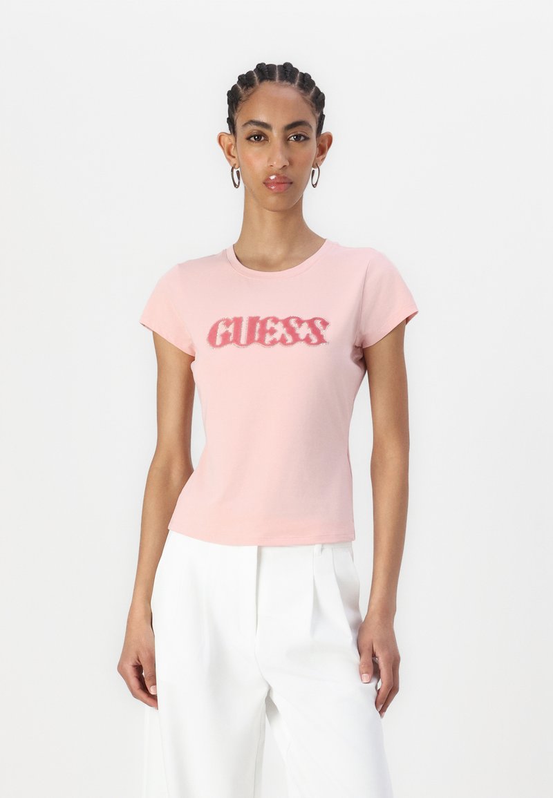 Šviesiai rožinė medvilninė marškinė su trumpomis rankovėmis, turi tekstūruotą tamsiai rožinę "GUESS" logotipą. Lygi medžiaga. Taisyklinga figūrai pritaikyta forma.