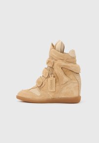 Baskets compensées en daim fauve avec trois sangles Velcro, bout perforé, talon clouté et une étiquette suspendue portant l'inscription "BRONX" sur fond blanc.