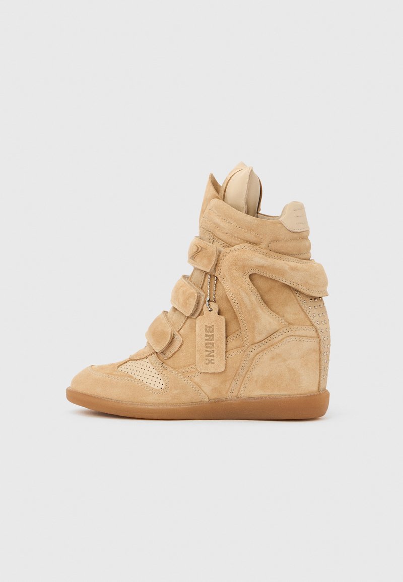 Baskets compensées en daim fauve avec trois sangles Velcro, bout perforé, talon clouté et une étiquette suspendue portant l'inscription "BRONX" sur fond blanc.