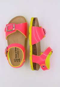 Sandales roses fluo avec boucle en argent, semelle en liège, semelle extérieure jaune et sangles ajustables. Fini lisse avec des accents contrastés.
