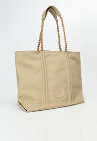Borsa tote beige realizzata in materiale testurizzato, con manici intrecciati e un dettaglio a logo circolare su un lato. Due accenti verticali di cucitura.