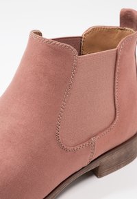 Rosa Wildleder-Ankle-Boot mit elastischen Seitenpanelen, einem niedrigen, gestapelten Holzabsatz und sichtbaren Nähdetails. Glatte Textur mit passgenauer Gestaltung.
